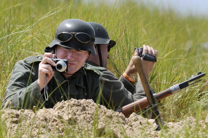 As Allied soldiers rush towards his position atop a sand dune, German World War II re-enactor Tony Kelly, from Chicago, pauses to take a picture of the advance during a re-enactment of D-Day on Saturday, June 20, 2009, at Tiscornia Beach in St. Joseph, Mich. The re-enactment marked the 65th anniversary of the Allied invasion of Europe on June 6, 1944.