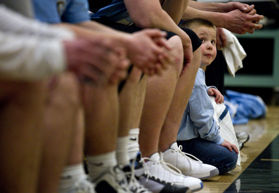 Kael Lissman, age 5, peers out from a line  of legs as he glances up at the scoreboard from the coaches' team bench during a charity basketball game between East coaches and the varsity boy's basketball team on Wednesday, March 23, 2011, at Cheyenne East High School. The friendly game benefited Isaac Salas, a Cheyenne South High School wrestler who broke his neck in November.